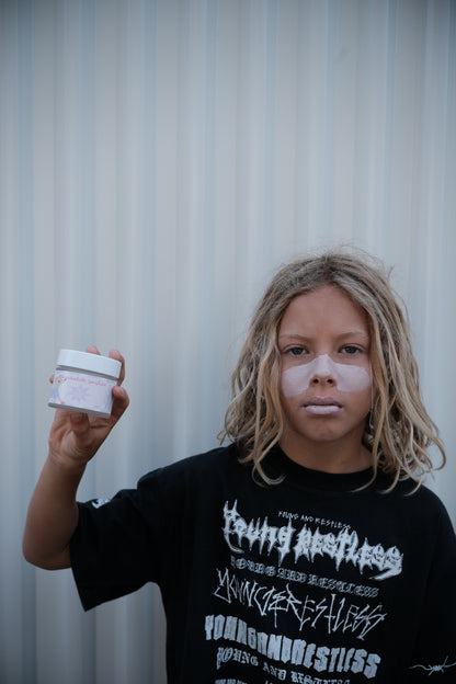 Child holding Glass Wholefoods Tallow Zinc Sun Balm with zinc applied to face outdoors