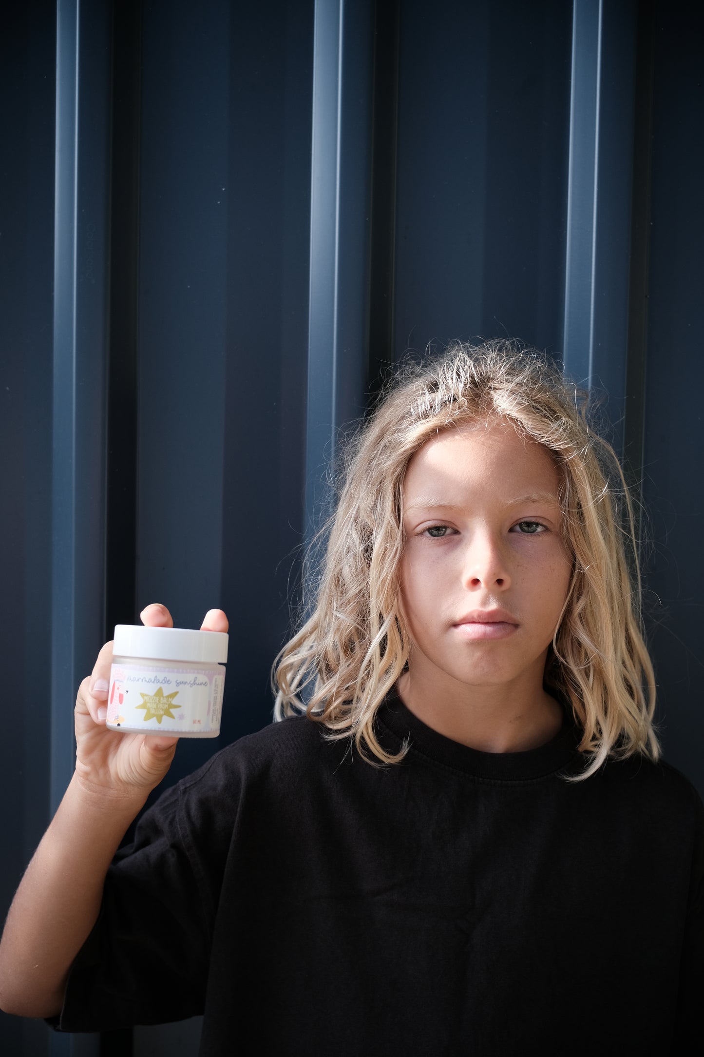 Child holding Glass Wholefoods Tallow Mosquito Balm jar against a dark studio background