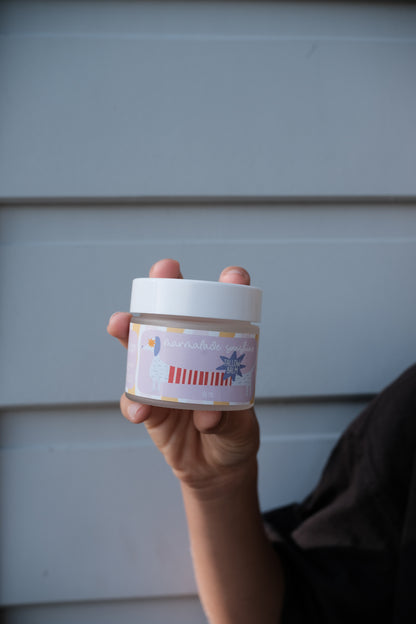 Hand holding Glass Wholefoods Tallow Balm jar with colourful label against a light blue wall