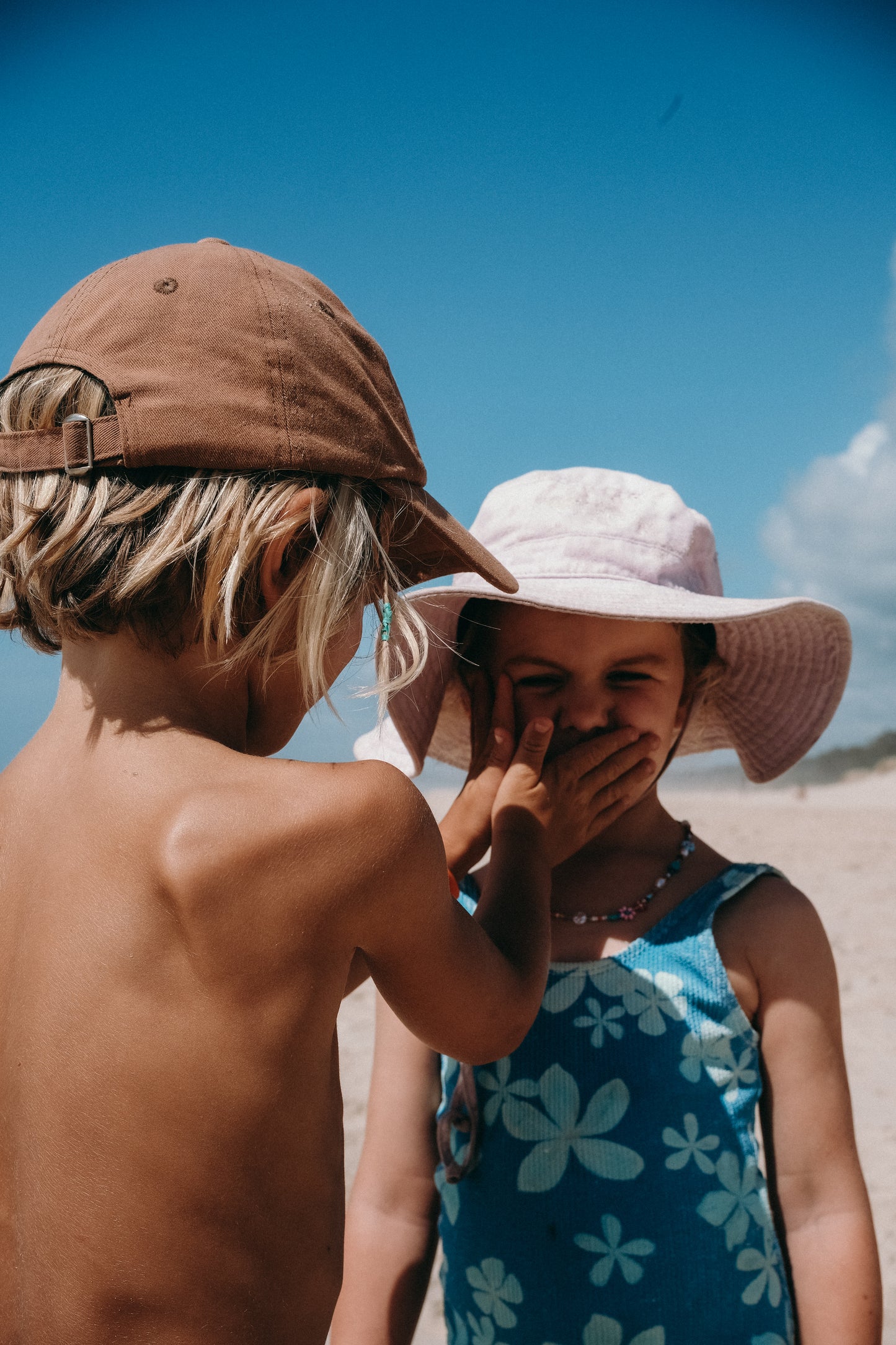 Two children at the beach applying Glass Wholefoods Tallow Zinc Sun Balm under a blue sky