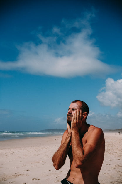 Man applying Glass Wholefoods Tallow Zinc Sun Balm on his face at the beach with blue sky