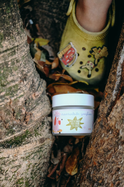 Glass Wholefoods Tallow Mosquito Balm jar nestled in tree bark outdoors with child's feet above