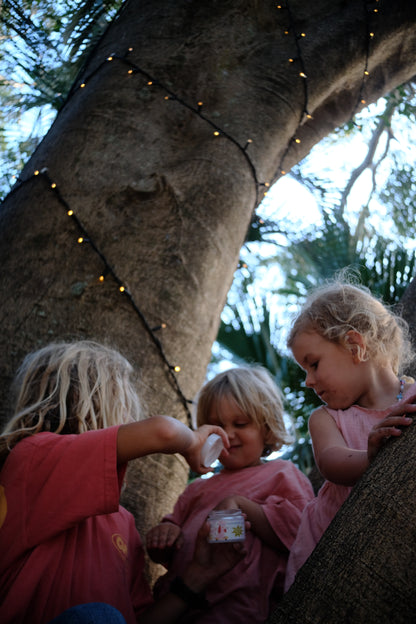 Children playing outdoors under a tree with string lights using Glass Wholefoods Tallow Mosquito Balm