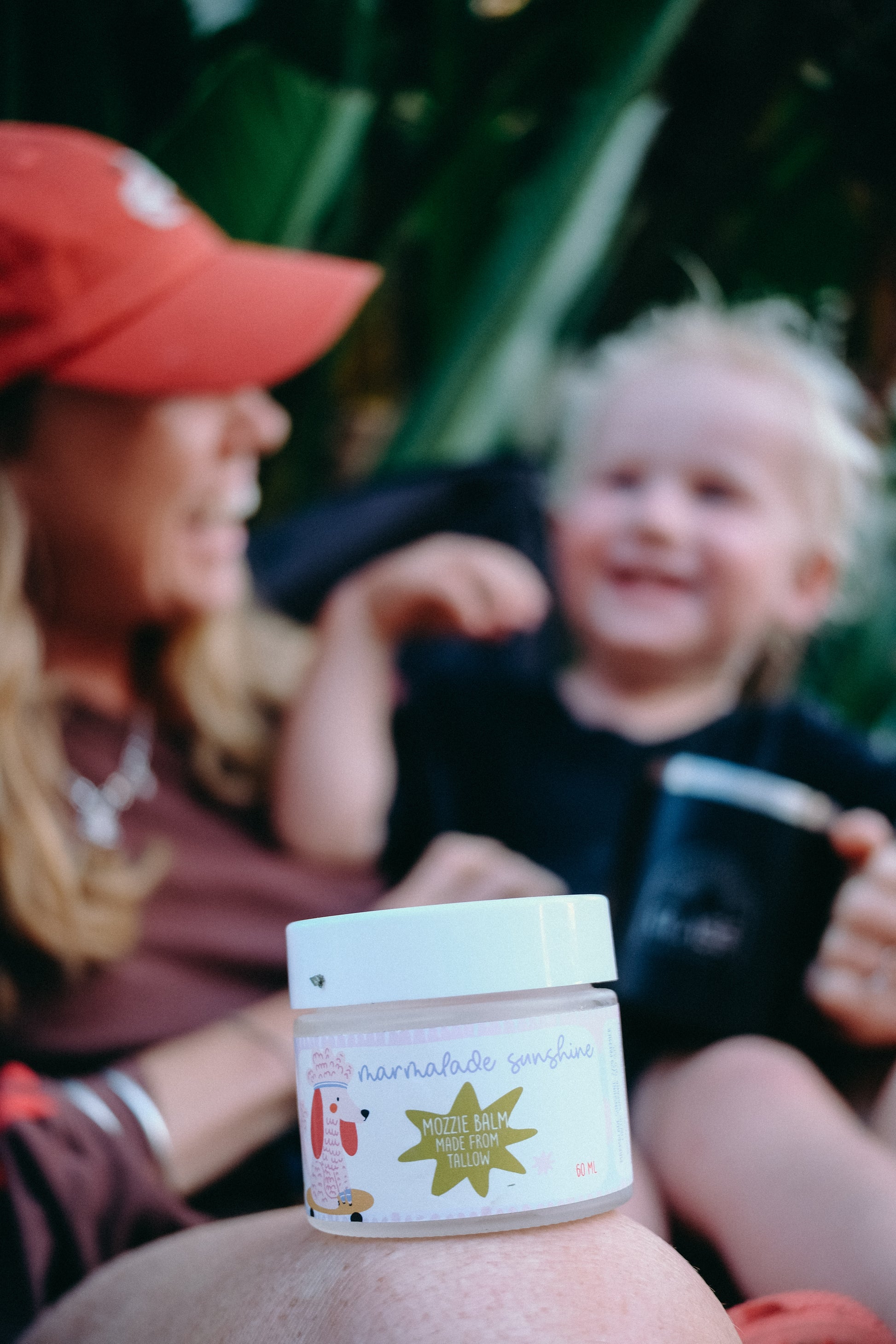Person holding Glass Wholefoods Tallow Mosquito Balm jar with a smiling child in an outdoor garden setting