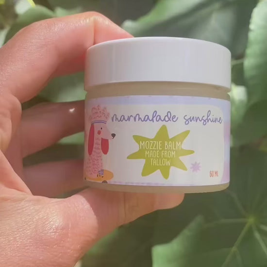 Close-up video of Glass Wholefoods Tallow Mosquito Balm jar held among green leaves outdoors