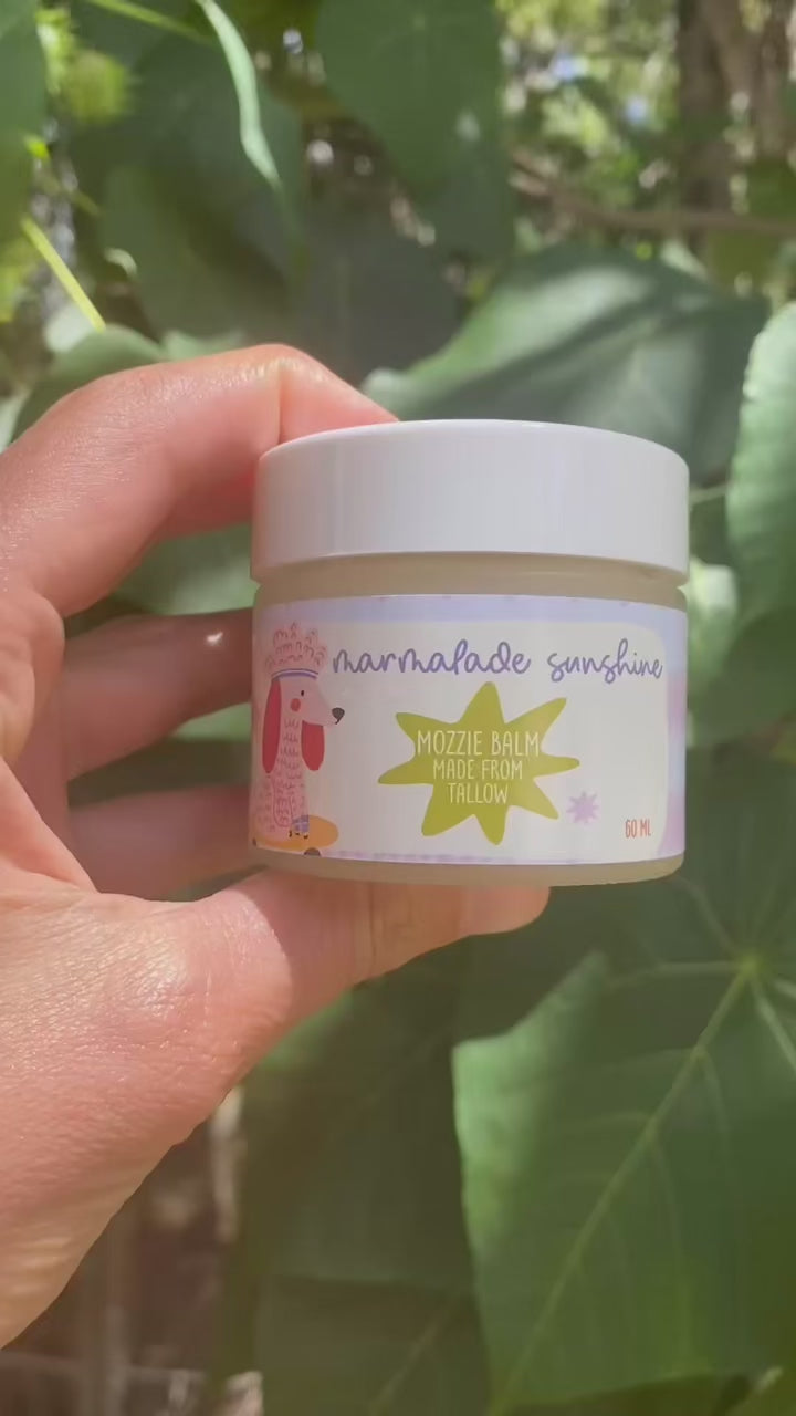 Close-up video of Glass Wholefoods Tallow Mosquito Balm jar held among green leaves outdoors
